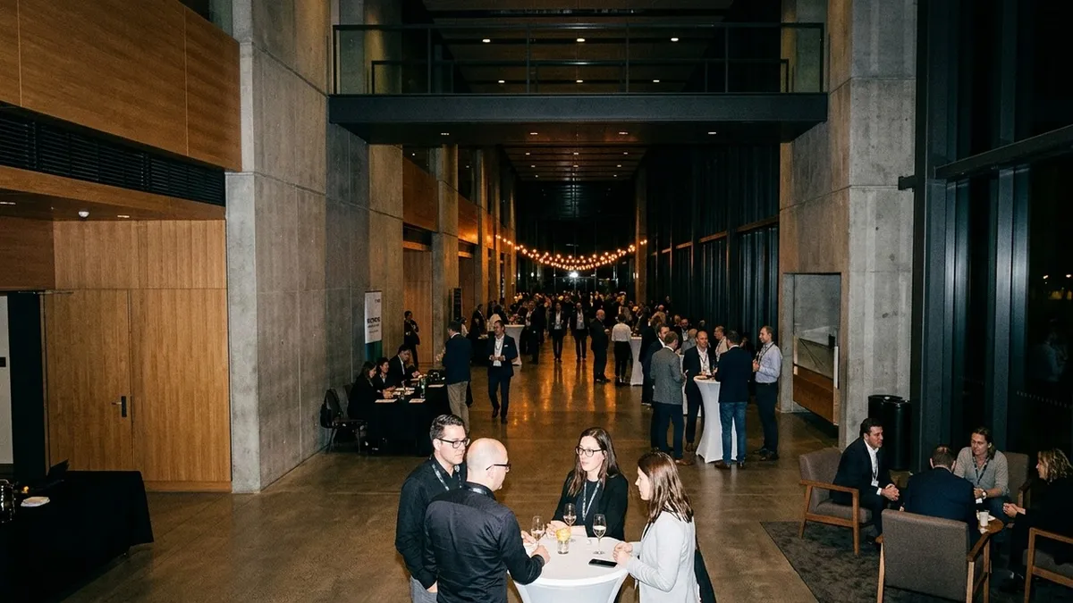 Abendlicher Networking-Empfang in einem großen Konferenz-Foyer: Teilnehmer im Gespräch an Stehtischen und in Lounge-Ecken, im Hintergrund eine Lichterkette über der Menge.